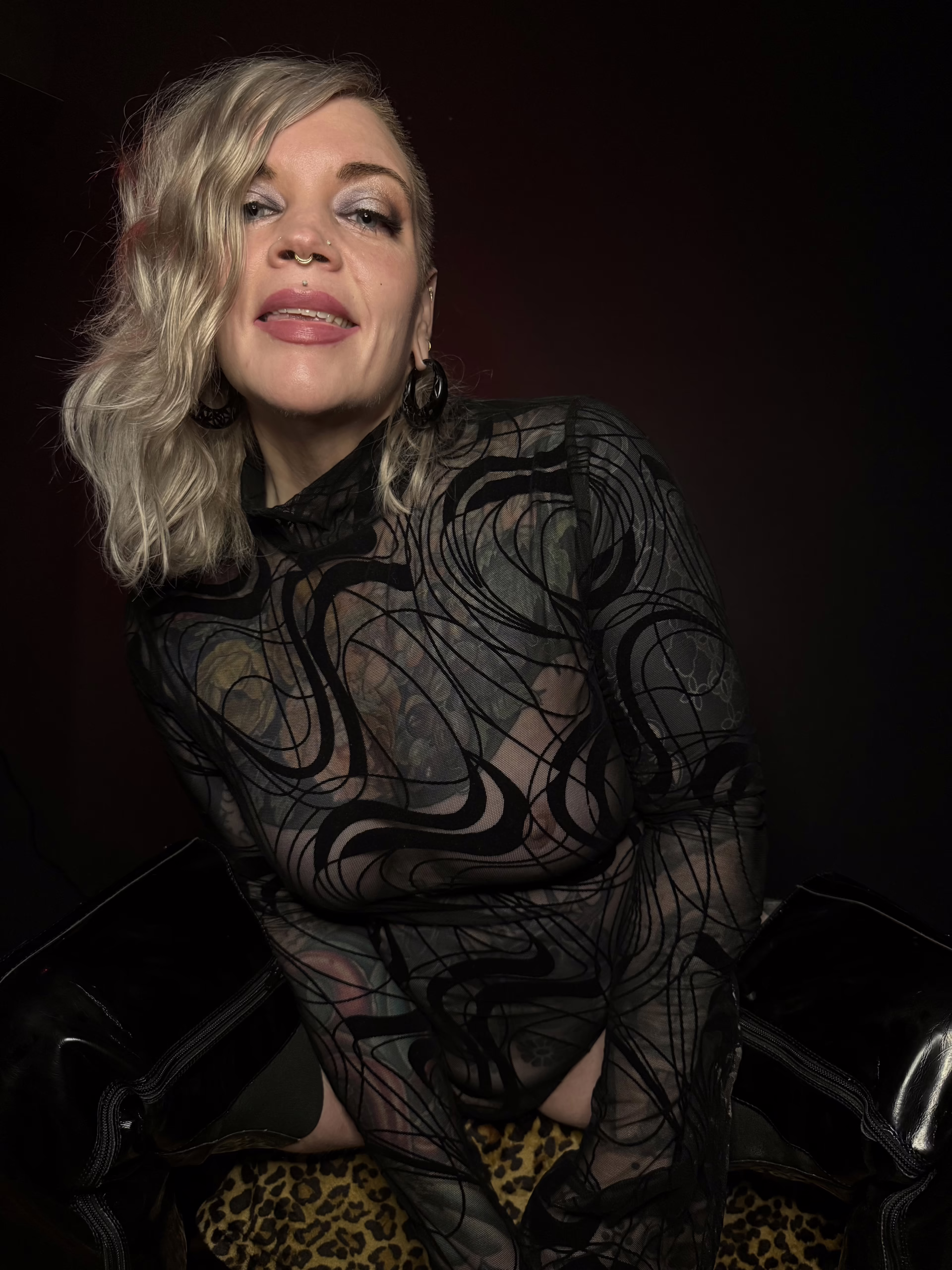 Erin Black is a strap-on and pegging escort in Chicago. She is wearing a black mesh bodysuit and wearing thigh high boots.